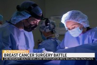 A still from a video of medical workers in surgical gowns and masks. Text on the screen reads, "Breast cancer surgery battle. CBS / KFF 国产精品视频 News investigation into reconstruction costs.