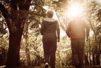 An active senior couple are jogging together through a nature trail. They have been photographed from behind.