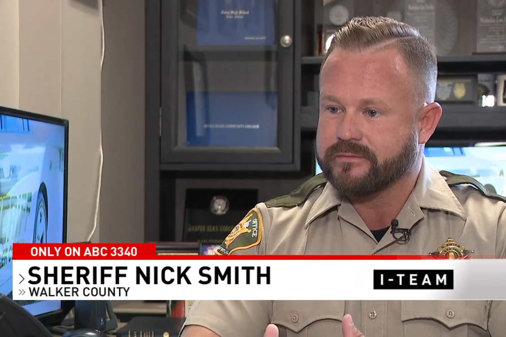 A photo of a man in a sheriff's uniform being interviewed on a TV news channel.