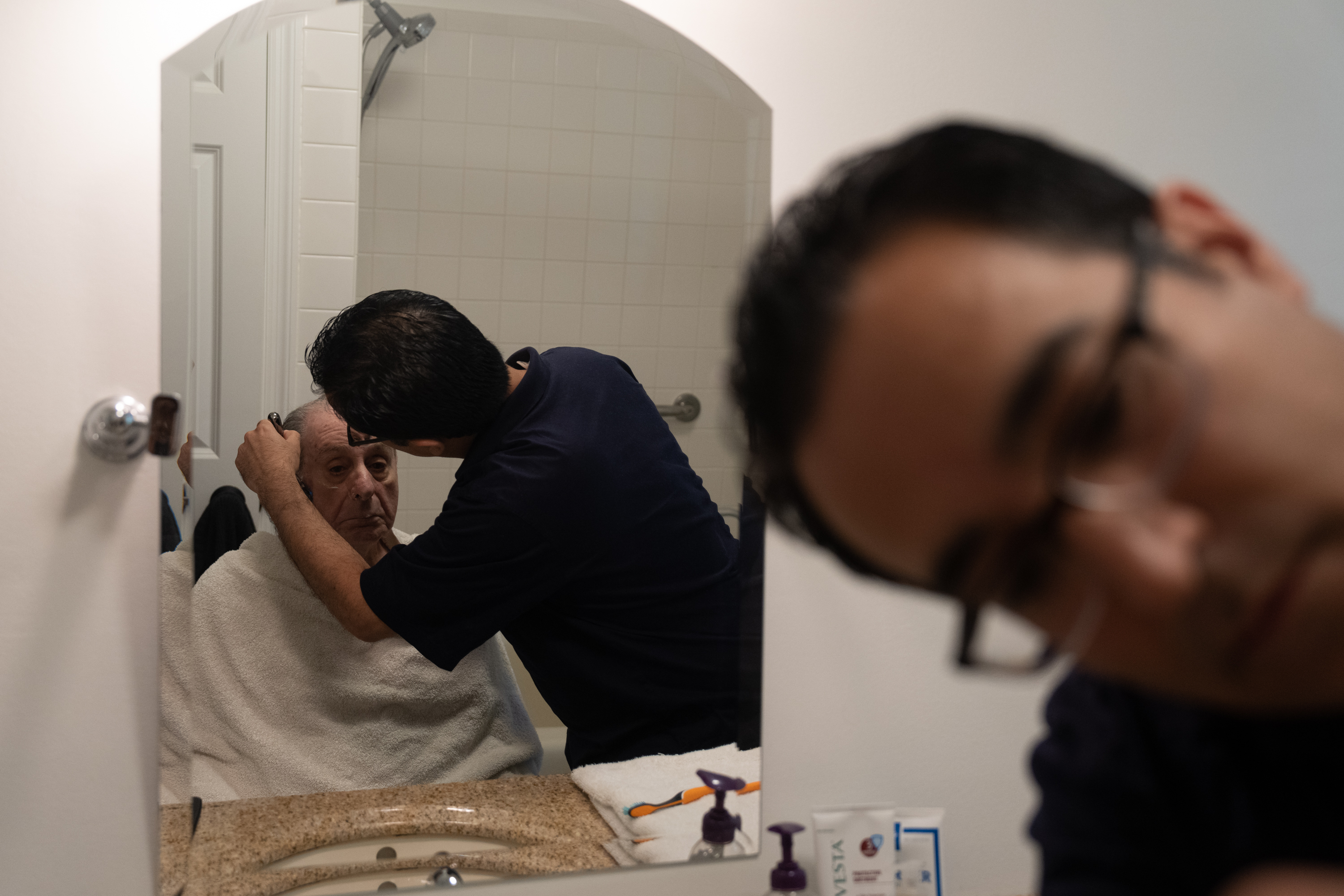 A photo of a man shaving his elderly father in front of a mirror.