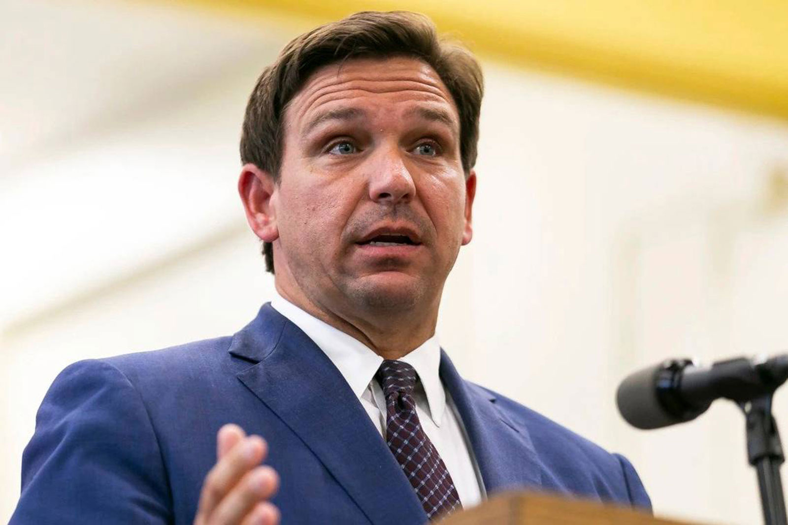 Florida Gov. Ron DeSantis in a suit and tie speaks from behind a lectern and gestures with his right hand.