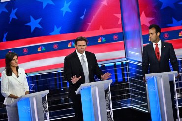 Three people stand behind lecterns on a debate stage. Former governor of South Carolina and United Nations ambassador Nikki Haley stands on the left, Florida Gov. Ron DeSantis is in the center and currently speaking, and entrepreneur Vivek Ramaswamy stands on the right.