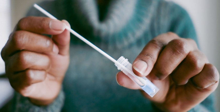 A photo of a woman's hands dipping a nasal swab into a small vial of solution as part of a covid-19 test.