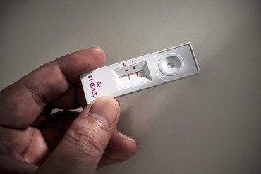 A photo of a person holding an at-home rapid test for covid-19 with a positive result.