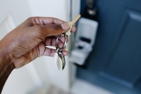 The photo shows a person holding house keys in their left hand. They prepare to unlock the door in front of them.